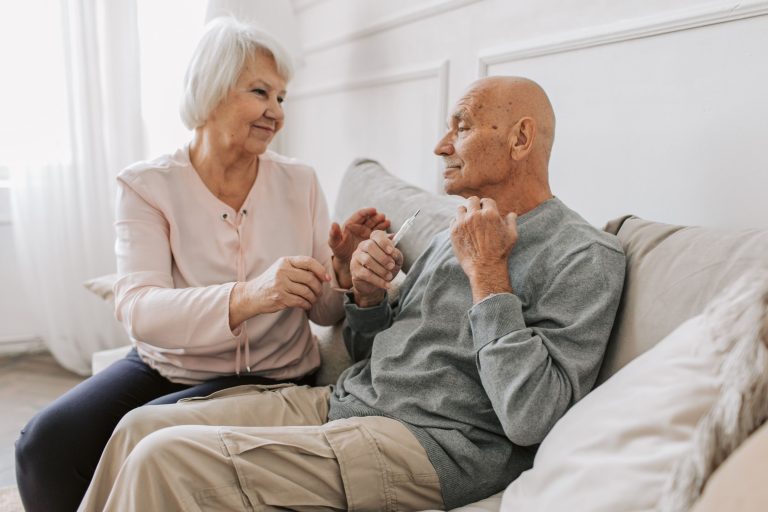 Zwei Senioren sitzen im Gespräch gemeinsam auf dem Sofa und lachen