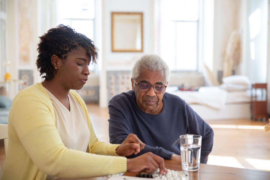 Pflegekraft hält die Hand einer Seniorin am Tisch